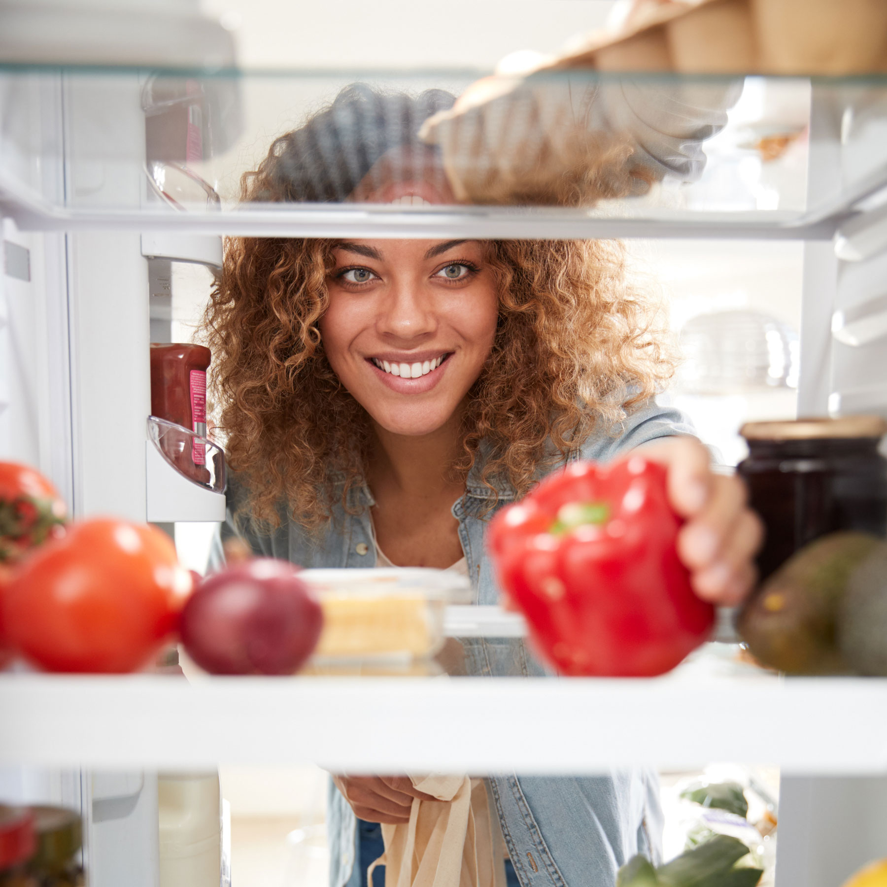 View Looking Out From Inside Of Refrigerator As Woman Opens Door And Unpacks Shopping Bag Of Food